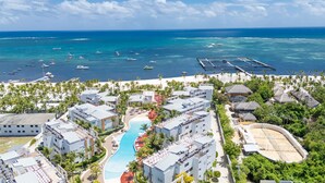 Un resort con piscina central, villas frente a la playa y un puerto deportivo con barcos.