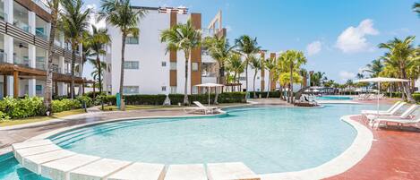 A swimming pool with lounge chairs, palm trees, and a modern building with balconies.