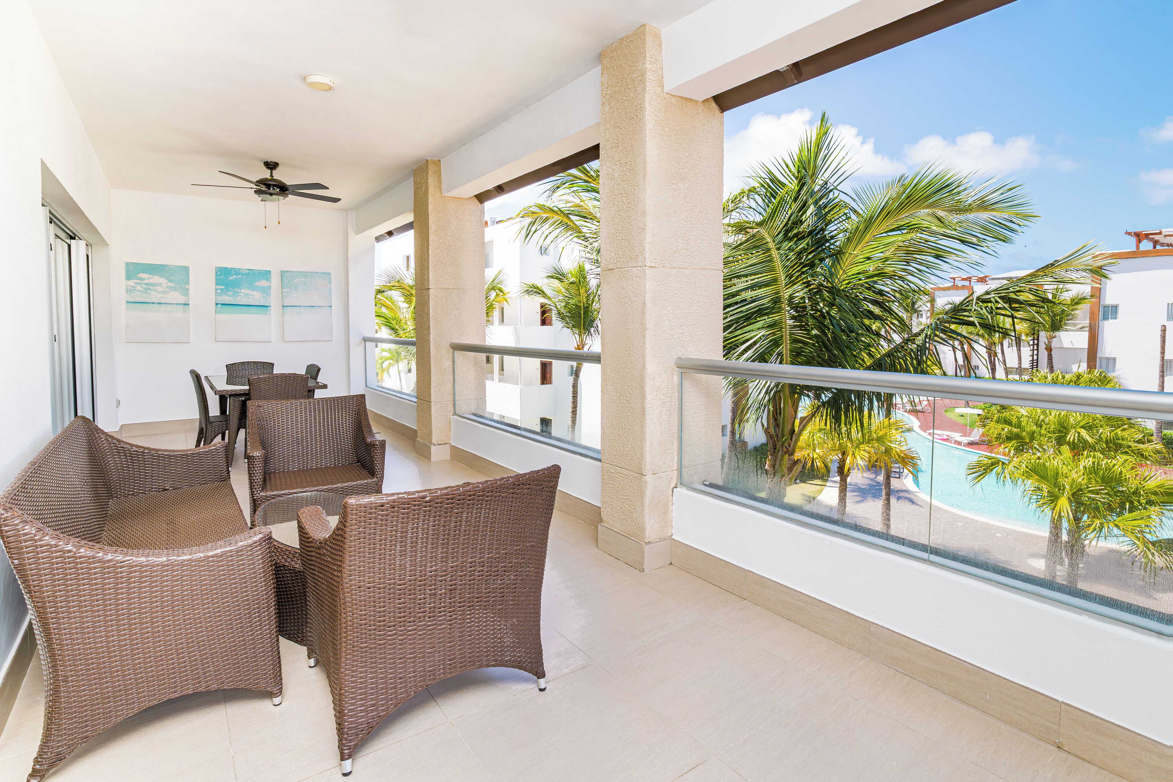 A balcony with wicker furniture, a ceiling fan, and a view of a pool and palm trees.