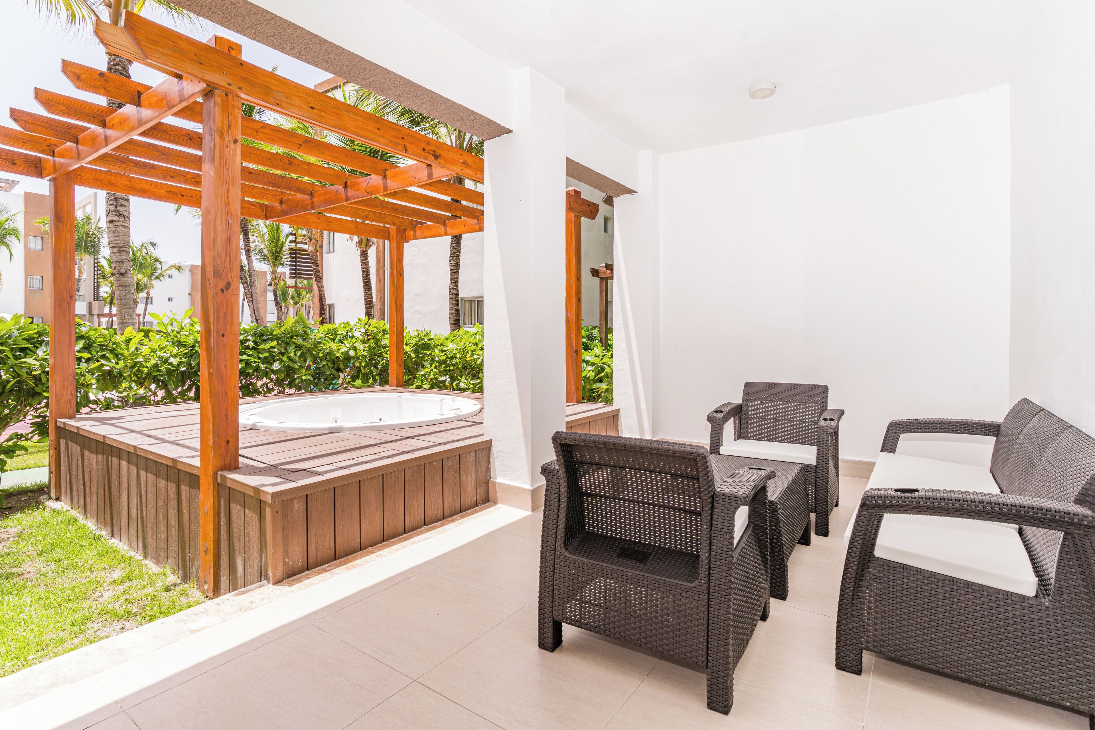 A patio area with a hot tub, wicker furniture, and a pergola.