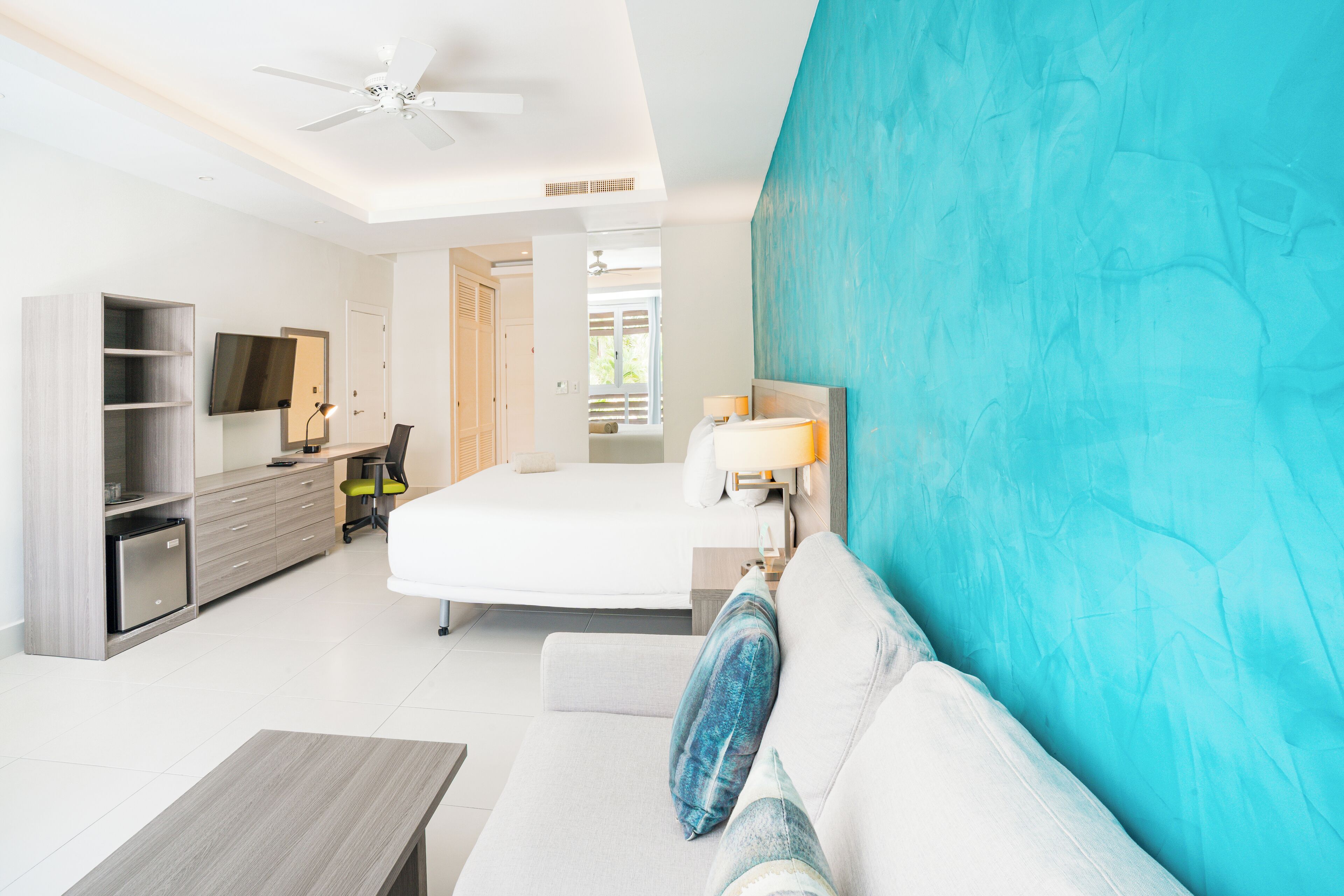 Habitación de hotel con cama, escritorio, silla, televisor y ventilador de techo.