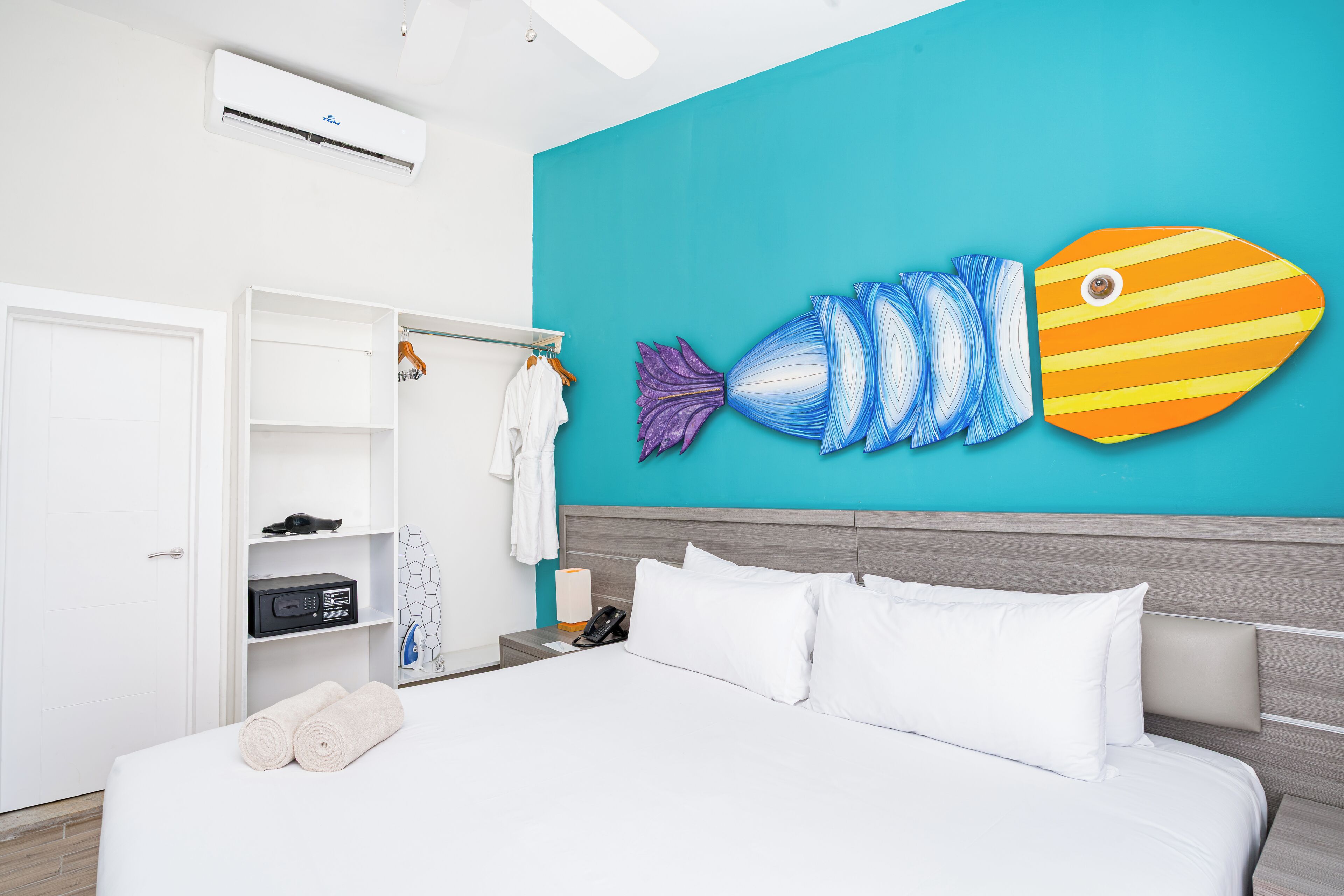 A hotel room with a bed, a wardrobe, a bathroom, and a wall with a fish mural.