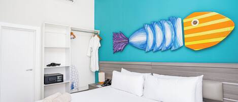 A hotel room with a bed, a wardrobe, a bathroom, and a wall with a fish mural.