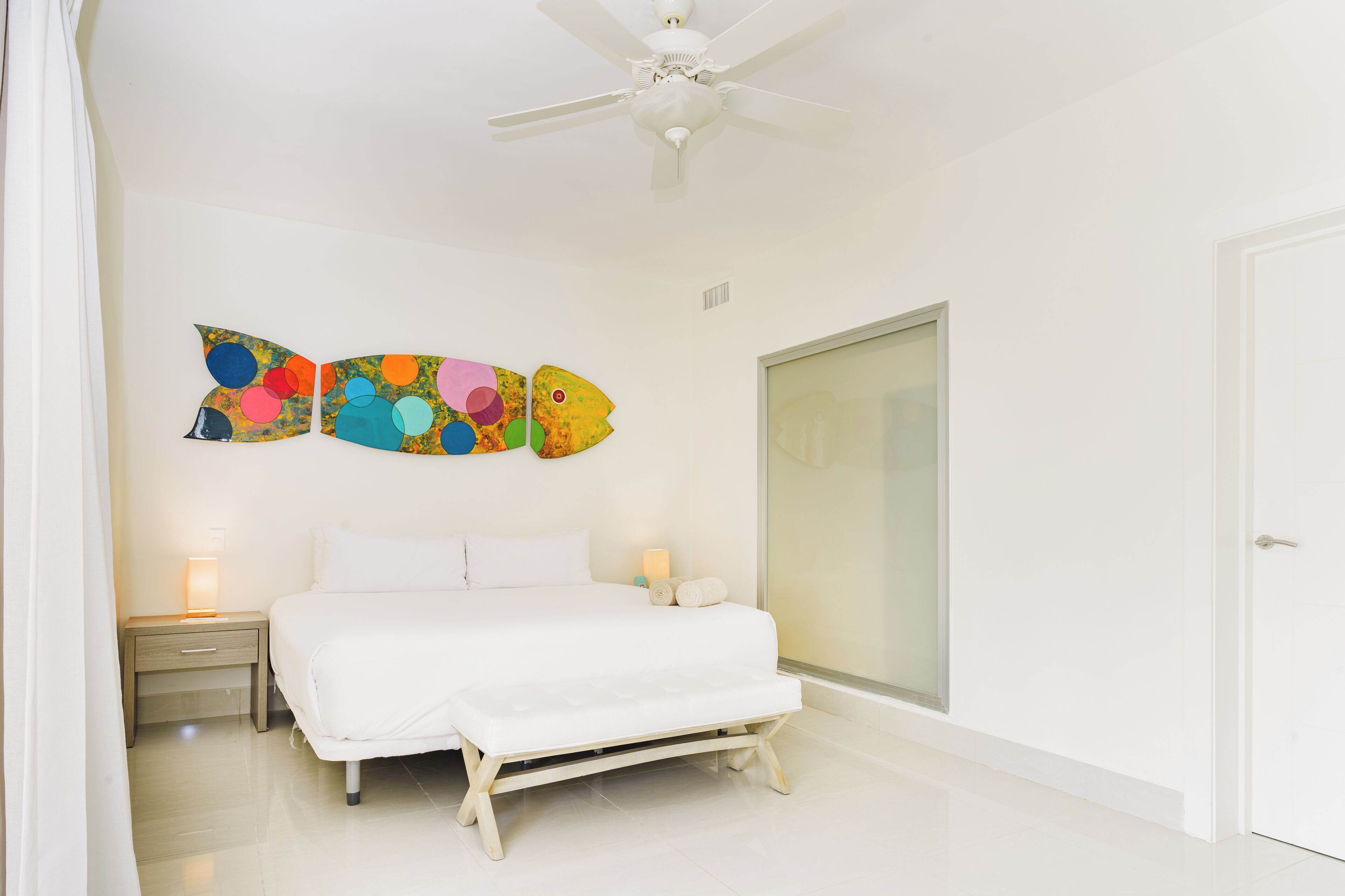 A bedroom with a bed, bedside tables, a ceiling fan, and a wall art piece.