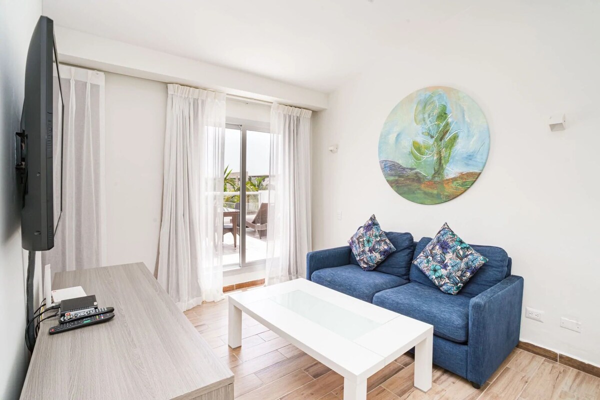 A living room with a sofa, a coffee table, a TV, and a painting on the wall.