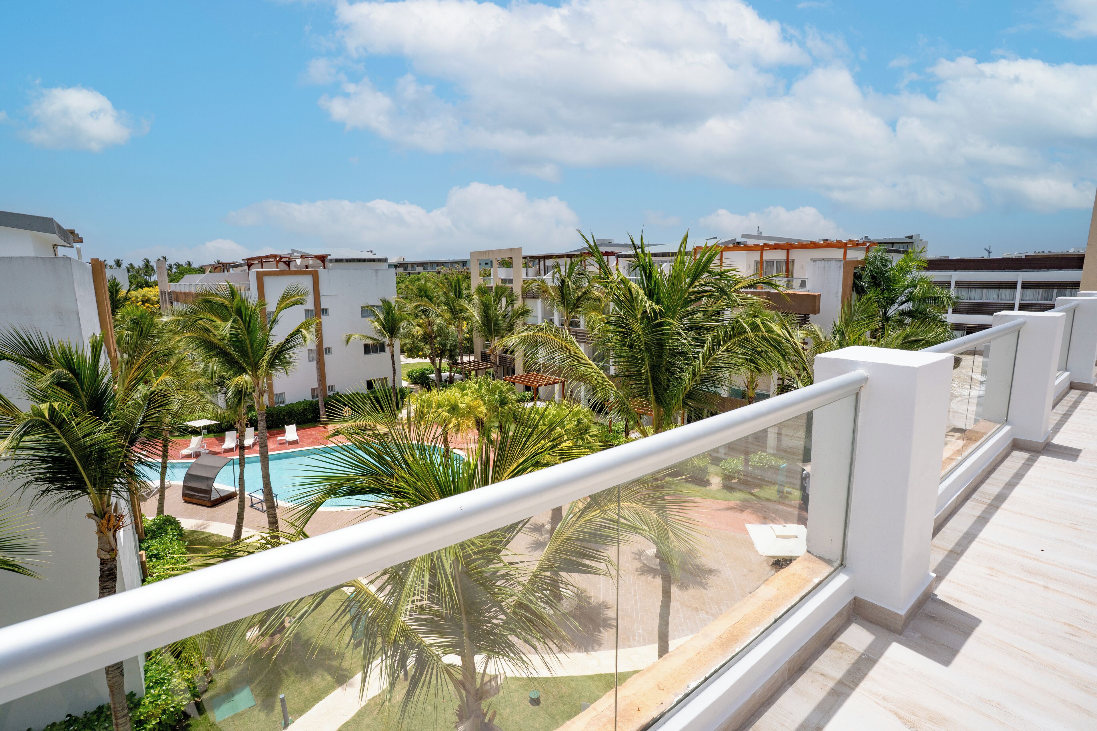 Een balkon met een zwembad, palmbomen en uitzicht op een woonwijk.