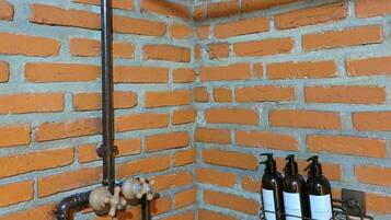 Esquina de una habitación con pared de ladrillo, una tubería negra y una estantería con botellas.