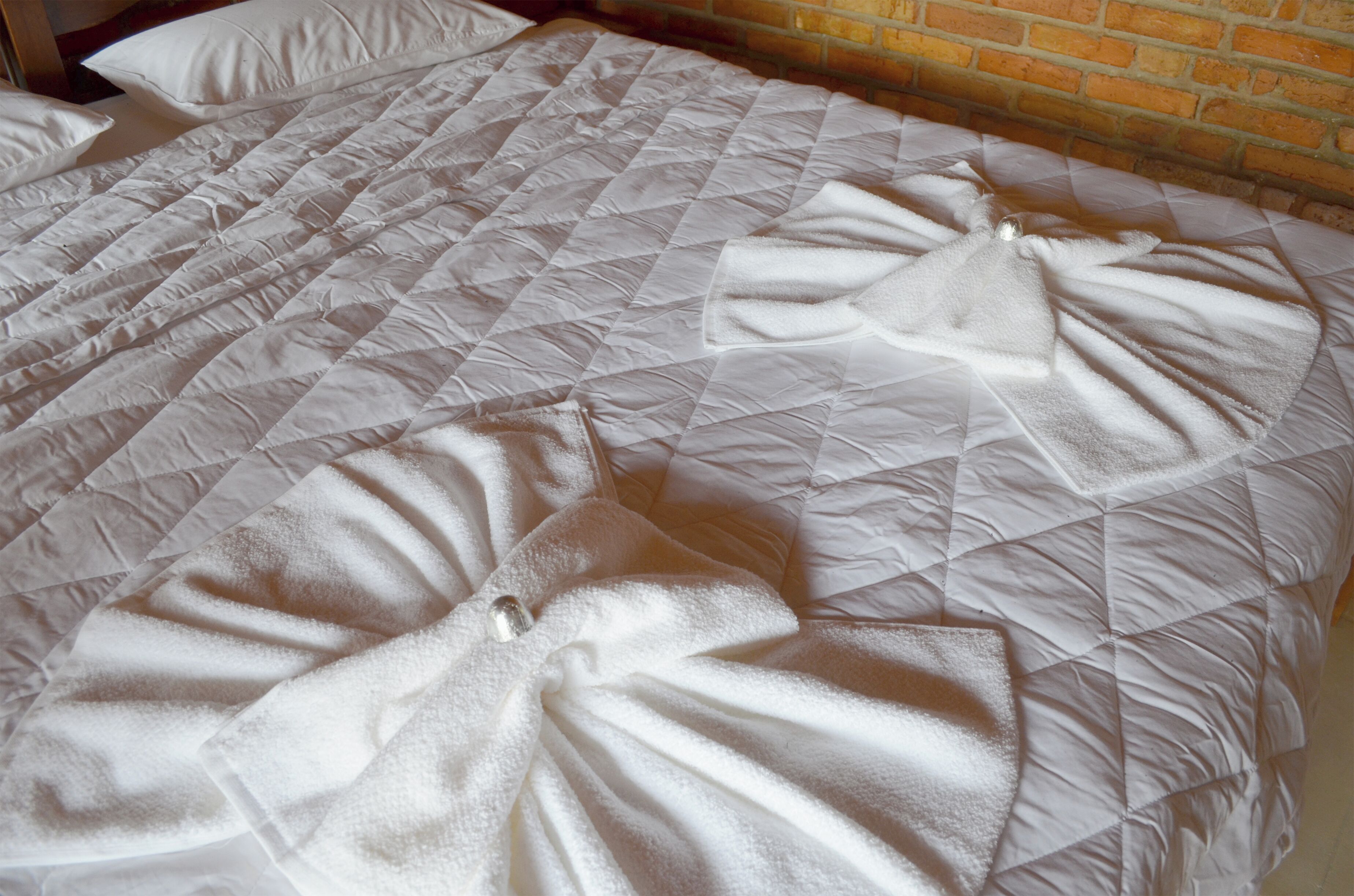 A bed with a quilted white duvet and pillows, a brick wall behind it, and a wooden headboard.