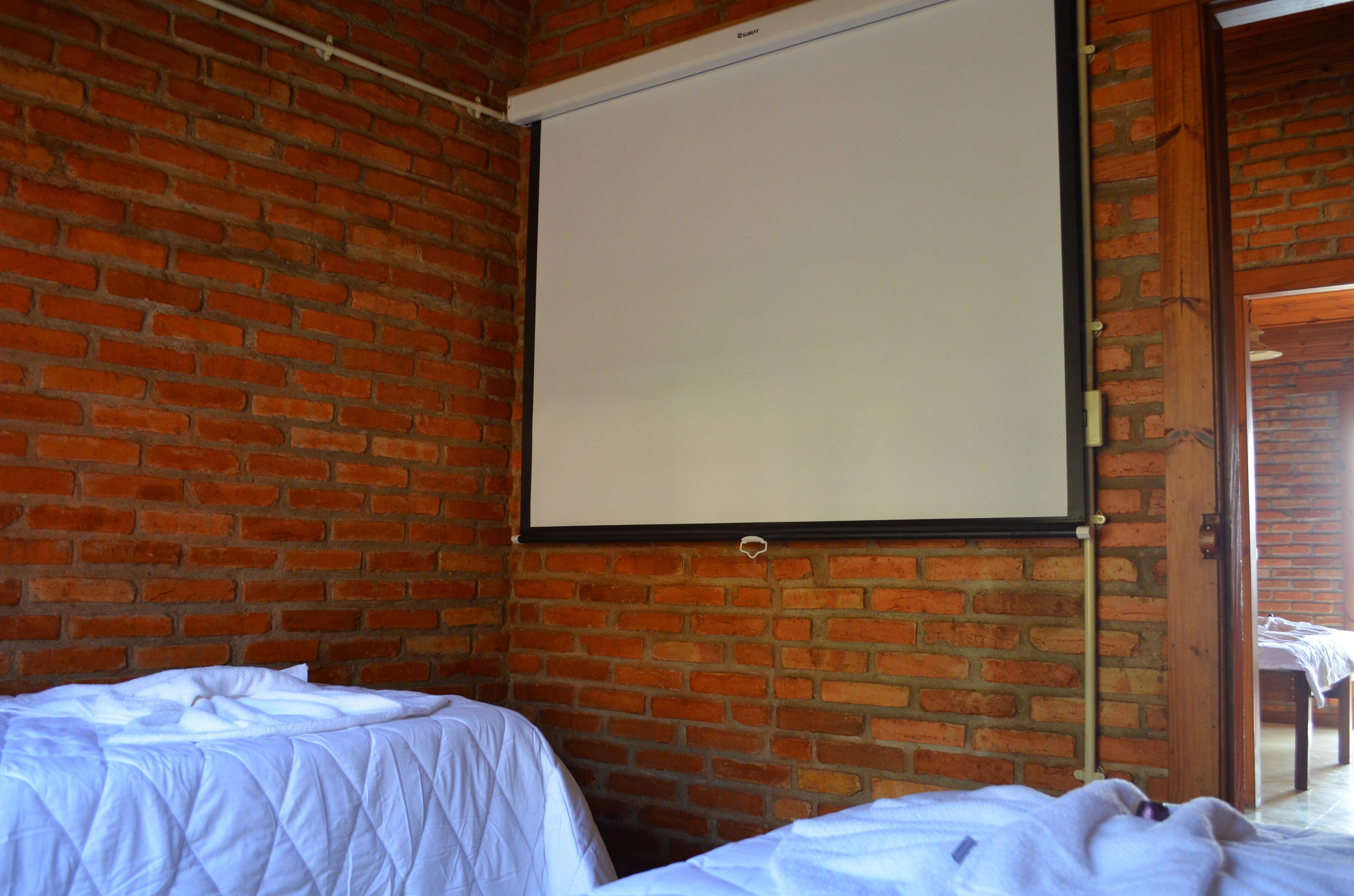 A room with a brick wall, a projector screen, and two beds with white bedding.