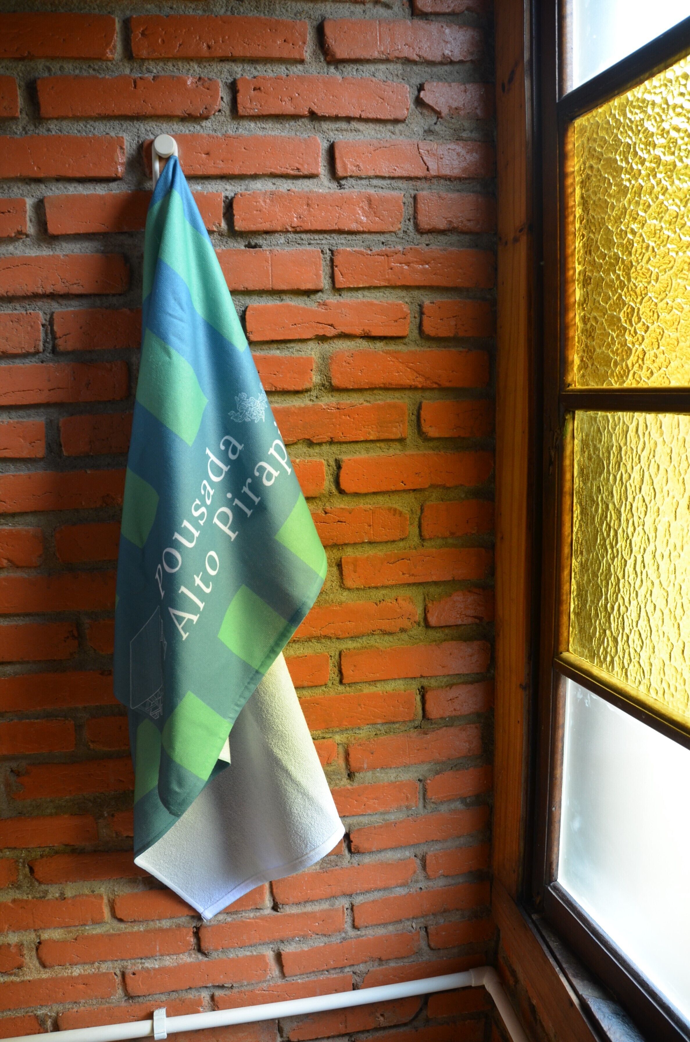 A towel hanging on a brick wall near a window with a textured glass pane.