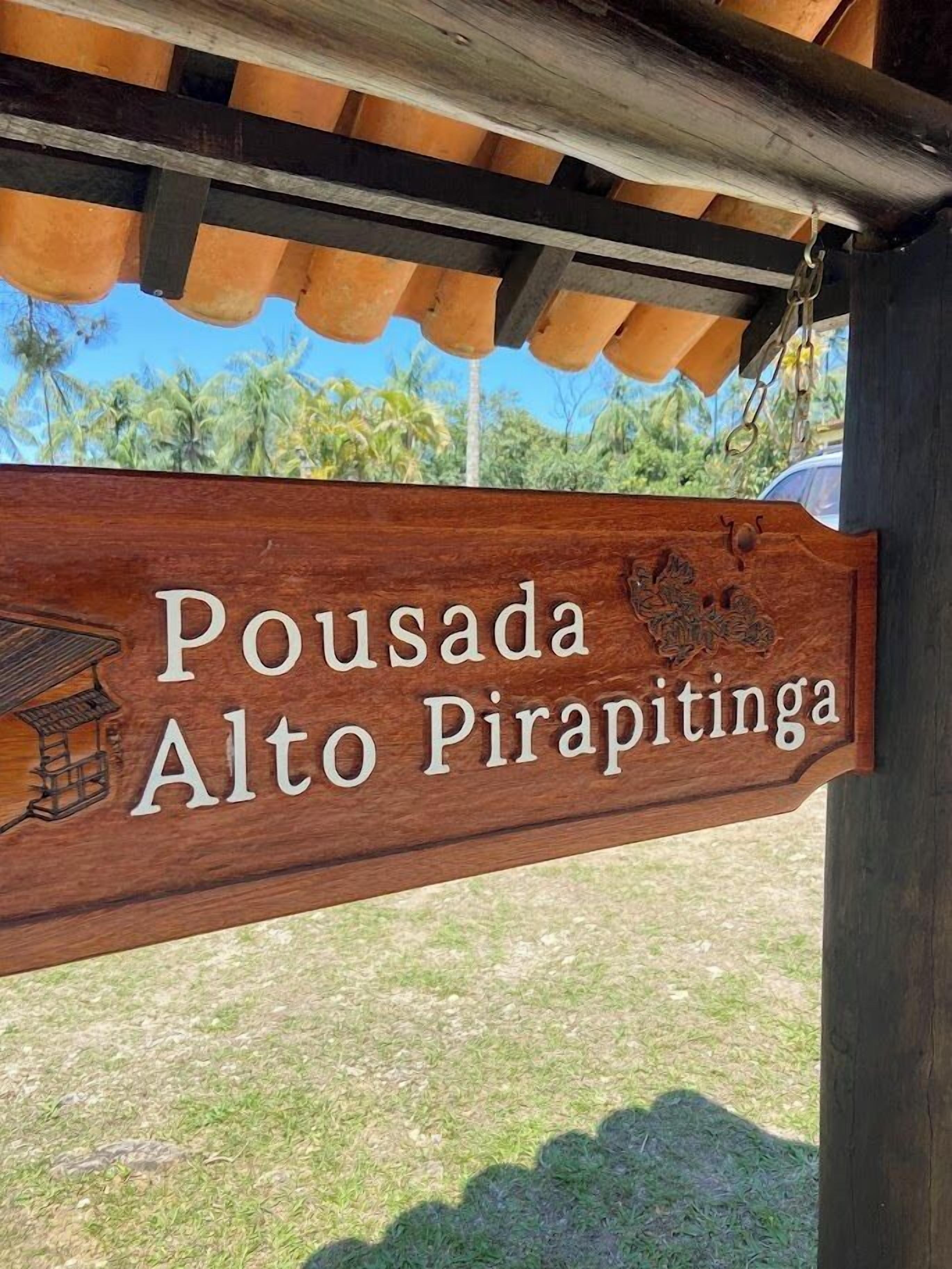A wooden sign with the text 'Pousada Alto Pirapitinga' and a small building illustration.