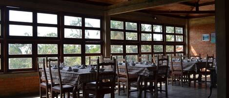 A spacious dining area with large windows, wooden tables, and chairs.