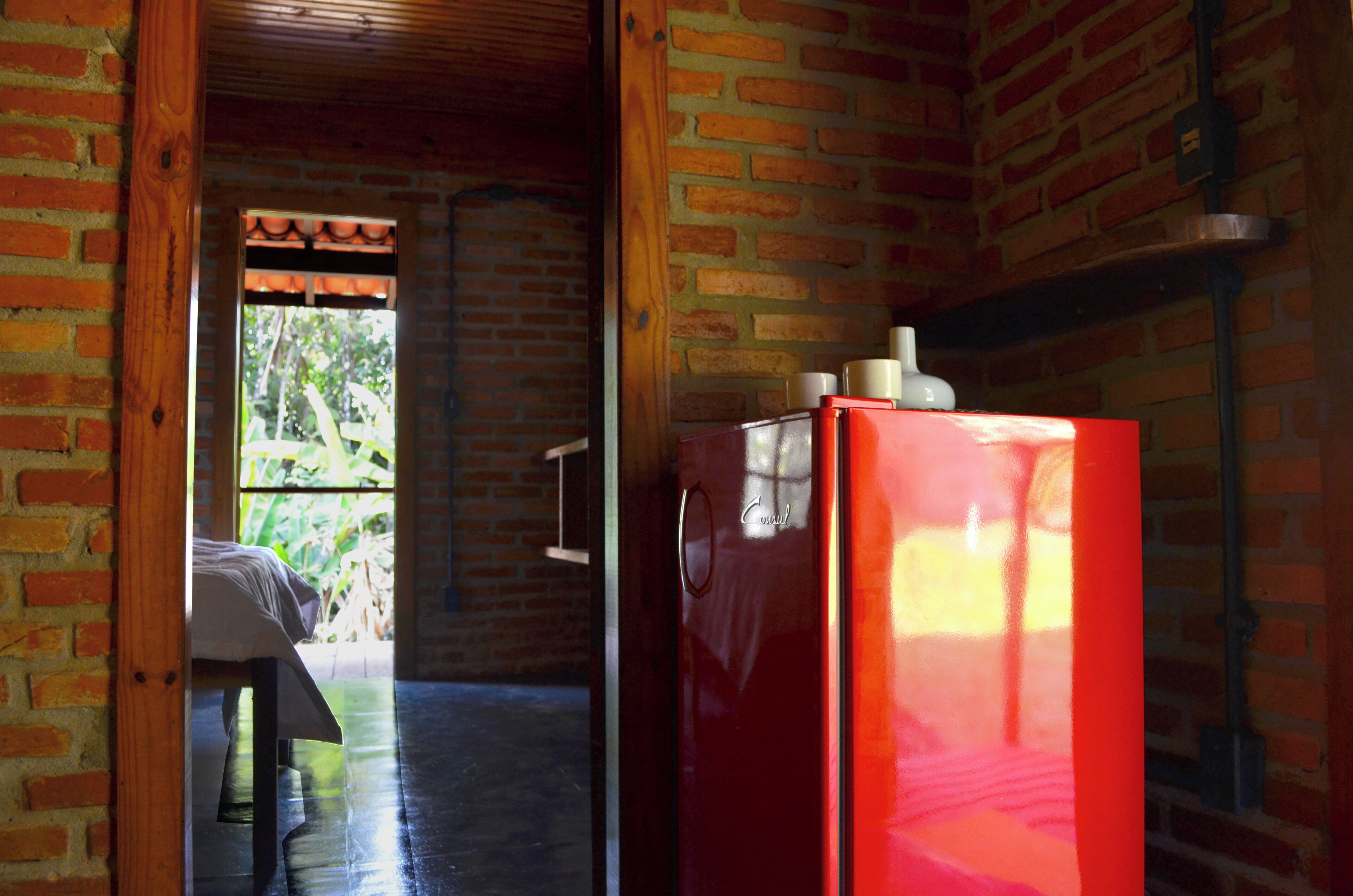 A room with a brick wall, a wooden door, and a red refrigerator.