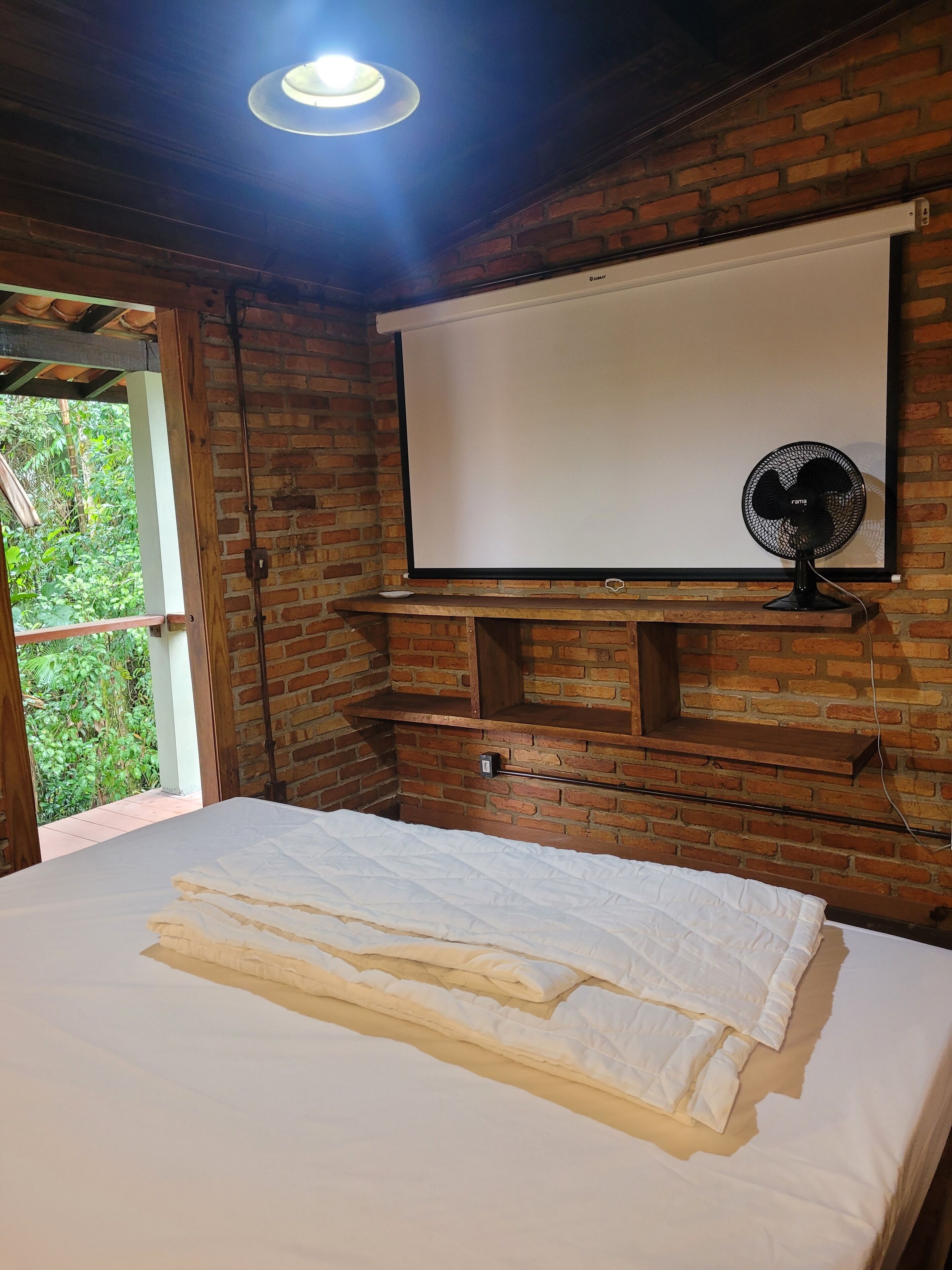 A room with a bed, a projector screen, and a fan.
