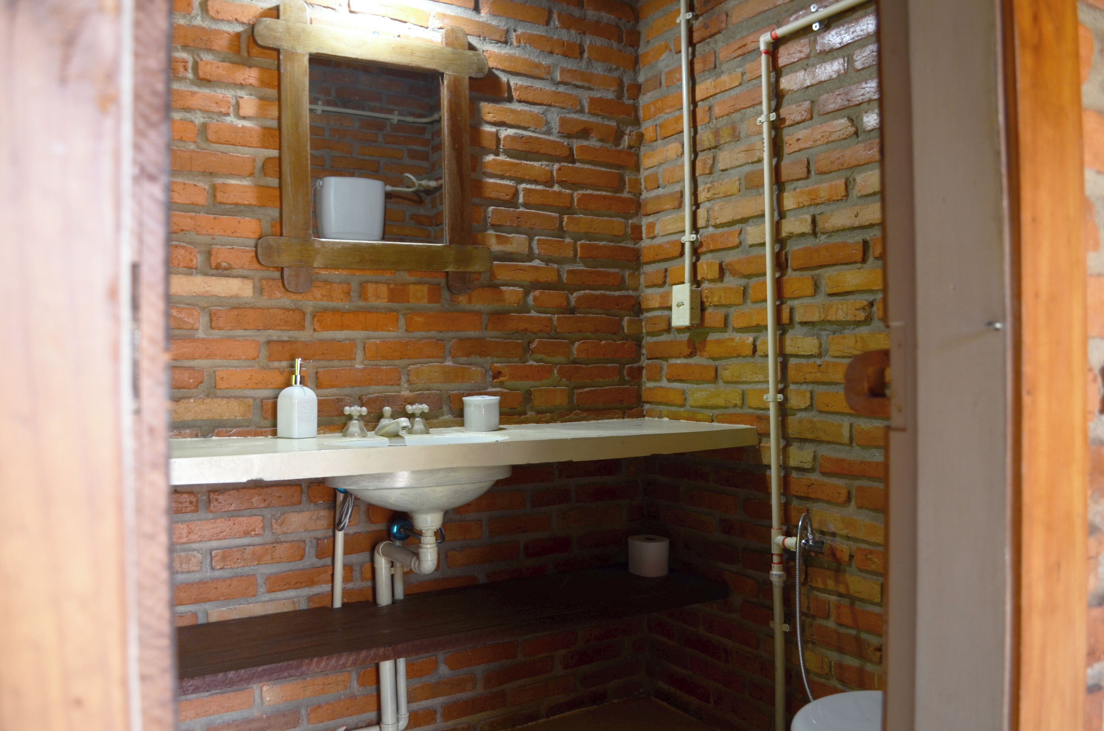 A bathroom with a brick wall, a white sink, a mirror, and a shower.