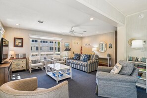 A well-lit living room with a large window, a ceiling fan, and a variety of seating options including a sofa, chairs, and a loveseat.