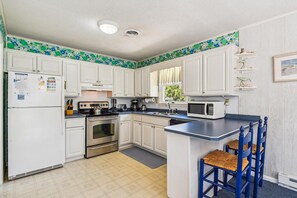 A kitchen with white cabinets, a stove, a microwave, and a sink. - Charming Oceanside Getaway! (South Bethany)