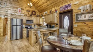 Una cocina de estilo rústico tipo cabaña, con paredes de madera, una isla central y una zona de comedor con una mesa y sillas de madera.