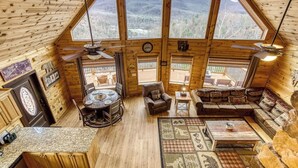L’intérieur d’un chalet en bois comprend un coin repas, un canapé et une vue sur les montagnes grâce à de grandes fenêtres.