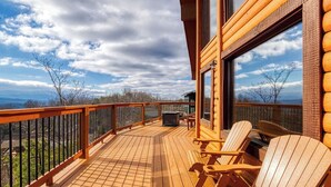 Una terraza de madera con sillas Adirondack, una mesa y vistas a las montañas.