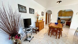 Una sala de estar con televisor, una mesa de comedor y una cocina a la vista a través de un arco.