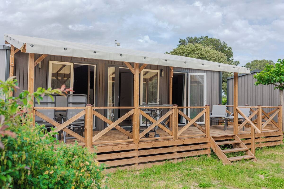 Una casa móvil con una terraza techada, ventanas amplias y barandilla de madera.
