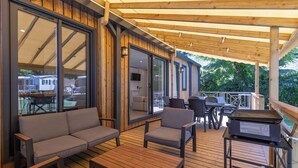 Una terraza cubierta al aire libre con piso de madera, un sofá, sillas y una parrilla.