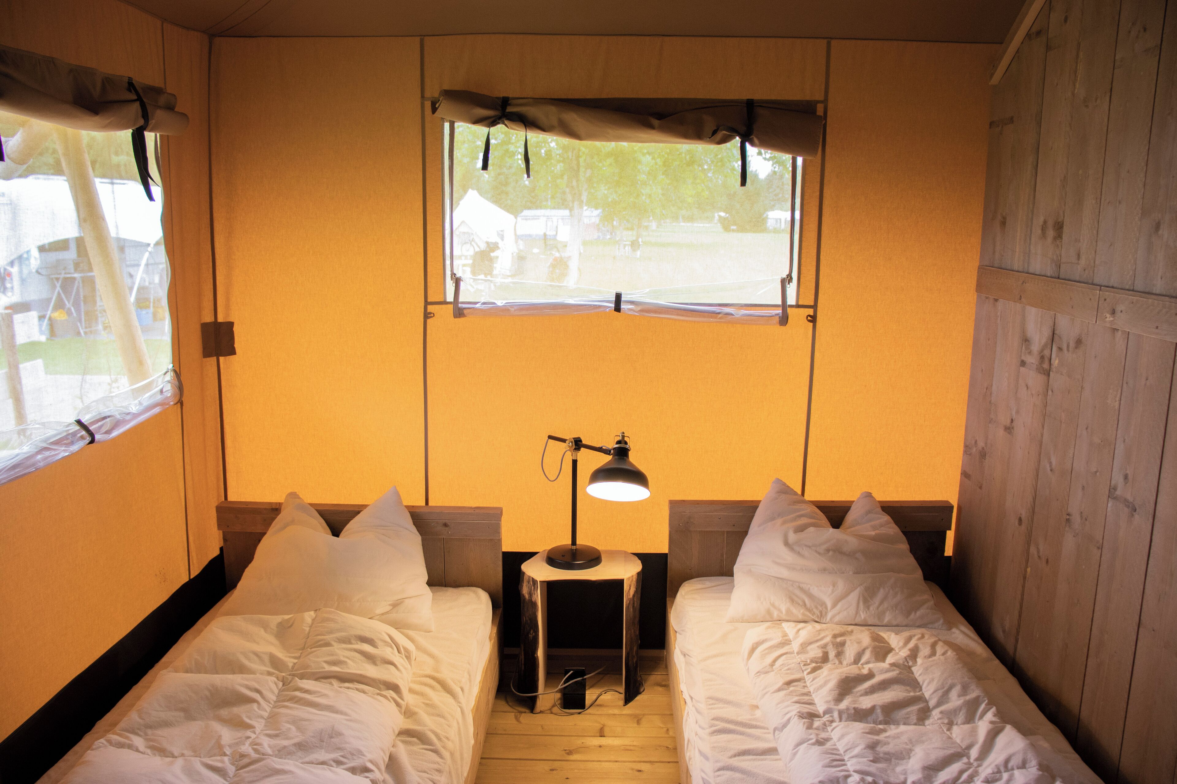 Una habitación pequeña y acogedora con dos camas individuales, una mesita de noche con lámpara y ventana con vistas al exterior.