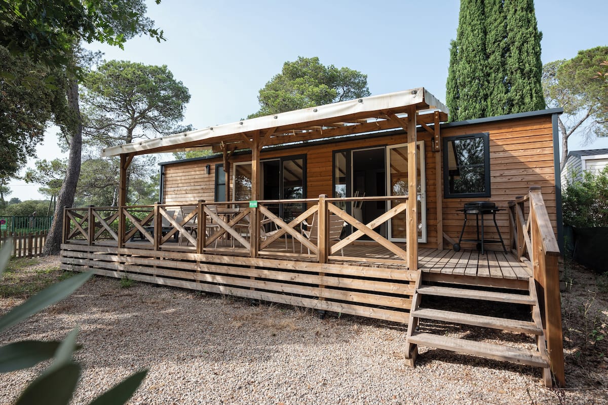 Una cabaña de madera con terraza, ventanas amplias y un espacio al aire libre cubierto.