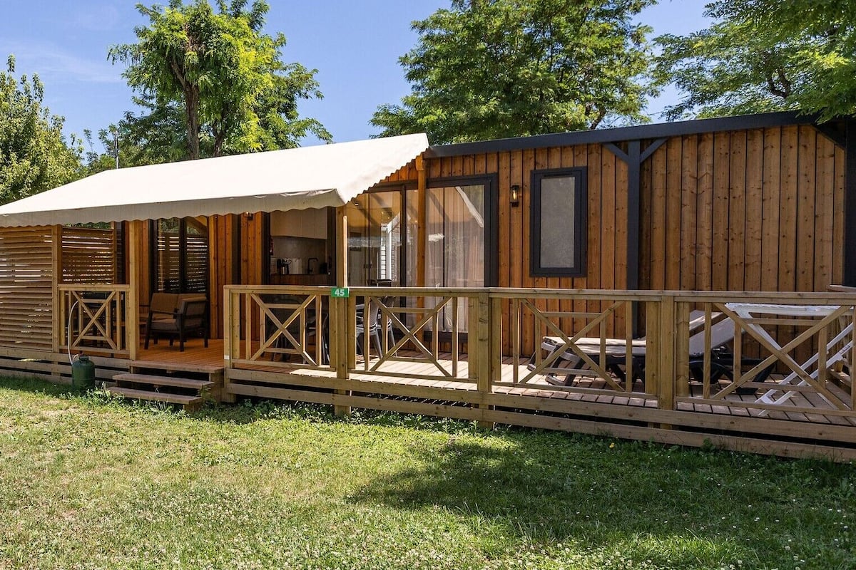 Una cabaña de madera con porche cubierto, mobiliario exterior y una pequeña mesa.