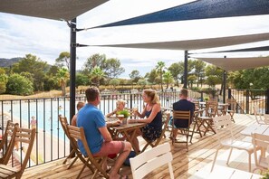 An outdoor dining area with tables and chairs overlooking a swimming pool. - RCN Domaine de la Noguière (Le Muy)