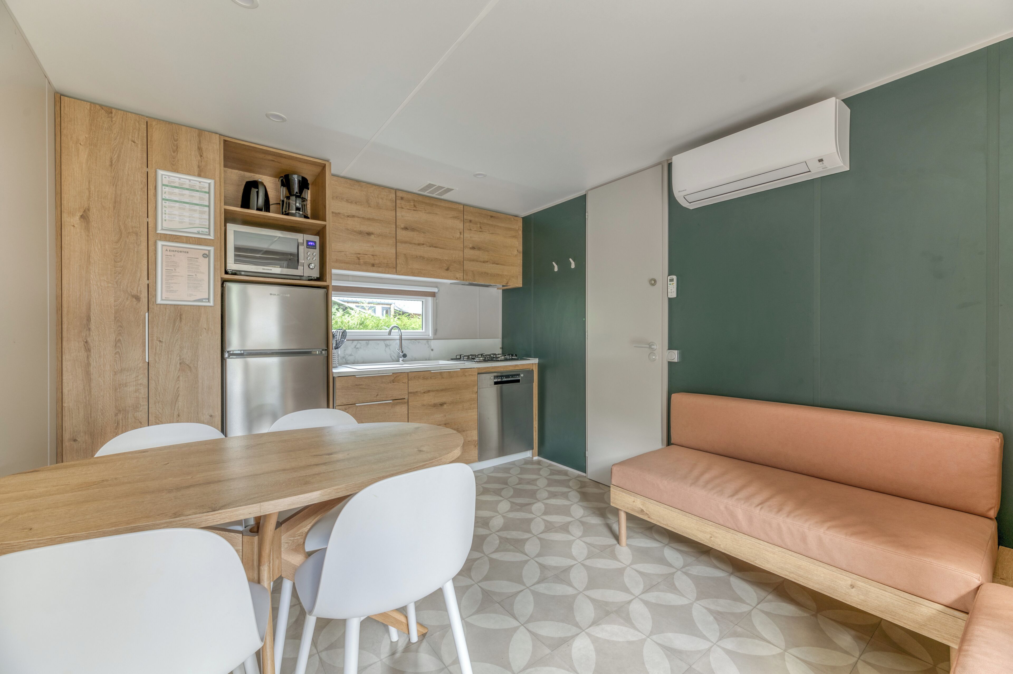 A compact kitchen with a built-in microwave, coffee maker, and dishwasher. There's a wooden dining table with chairs and a cushioned bench.