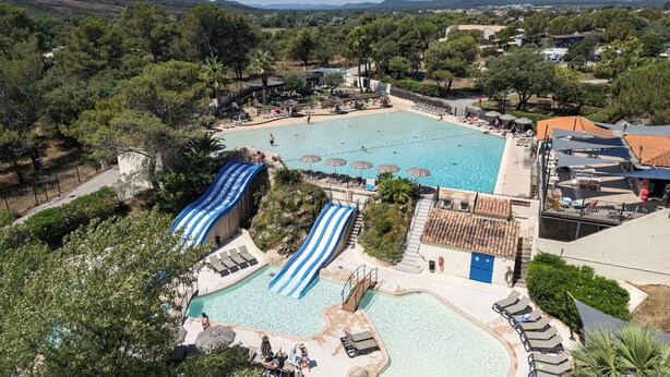 Una gran piscina al aire libre con tobogán, rodeada de zonas de descanso y sombrillas.