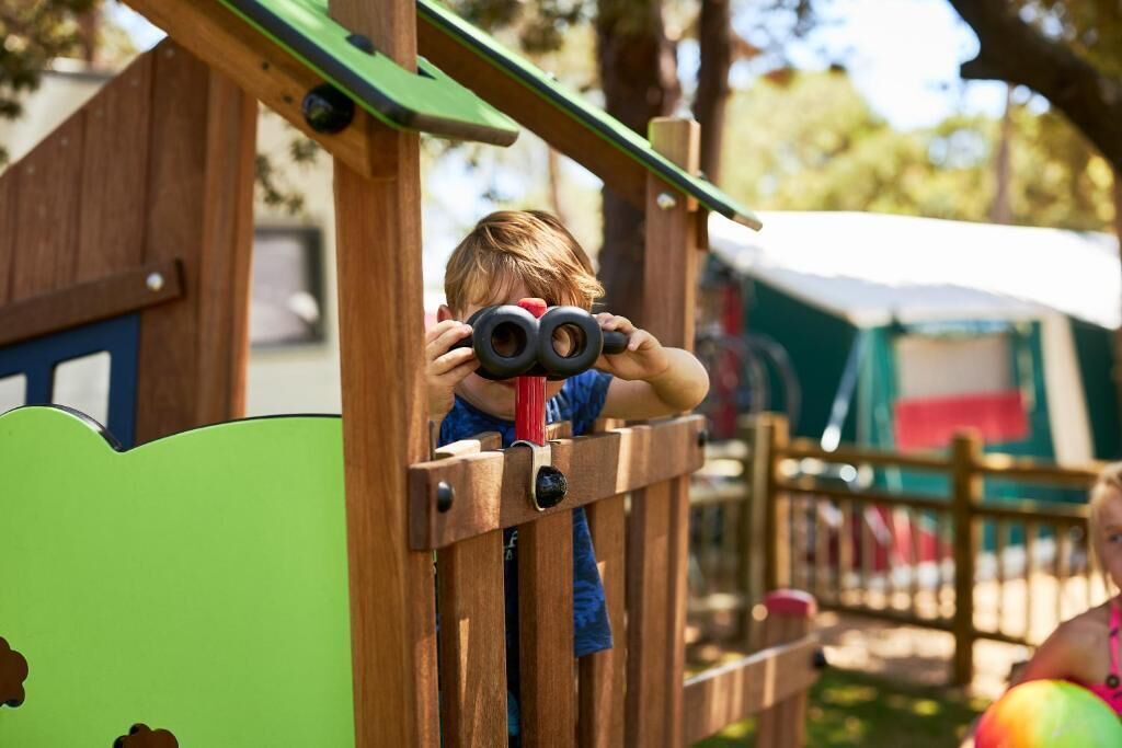 Un enfant utilise des jumelles sur une structure de jeu en bois.