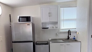 Una cocina compacta equipada con refrigerador, microondas, lavavajillas y un pequeño basurero.