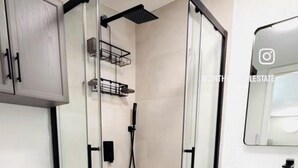 Un baño moderno con cabina de ducha de vidrio, inodoro y tocador con espejo.