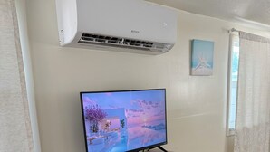 Una habitación con aire acondicionado, un televisor sobre una mesa blanca y un cuadro en la pared.