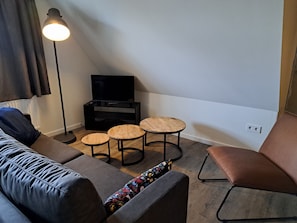 A modern living room with a sofa, two small round tables, a television, and a floor lamp.