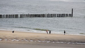 En strand med en vågbrytare av trä och människor som promenerar längs strandkanten.