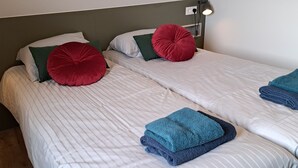 En dubbelsäng med randigt sänglinne, två röda kuddar och hopvikta handdukar.