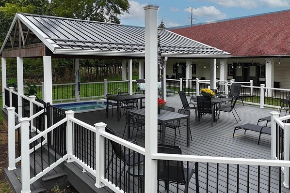 Une terrasse extérieure couverte, dotée de tables et de chaises, une piscine et, au fond, un bâtiment avec un toit rouge.