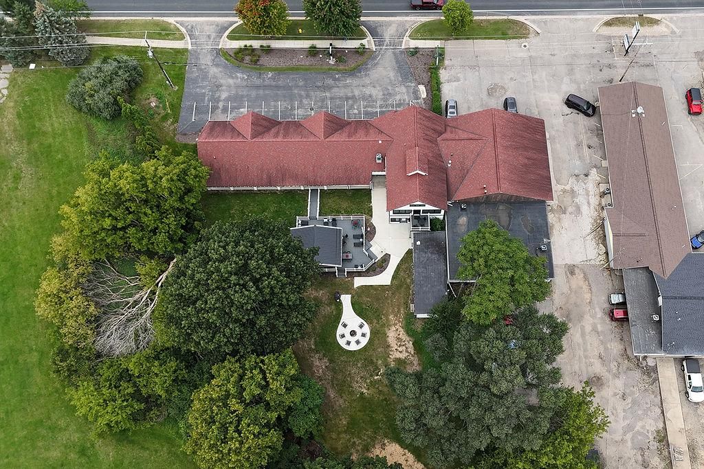 An aerial view of a residential area with a house featuring a red roof, a driveway, and a circular outdoor seating area.