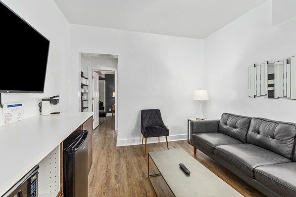 Een moderne woonkamer met een grijze bank, een salontafel, een televisie en een bijzettafeltje met een lamp.