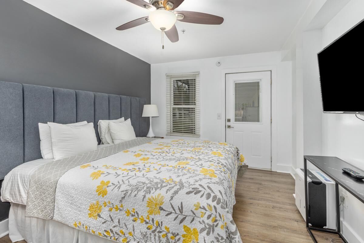 A bedroom with a bed, a ceiling fan, a TV, and a door.