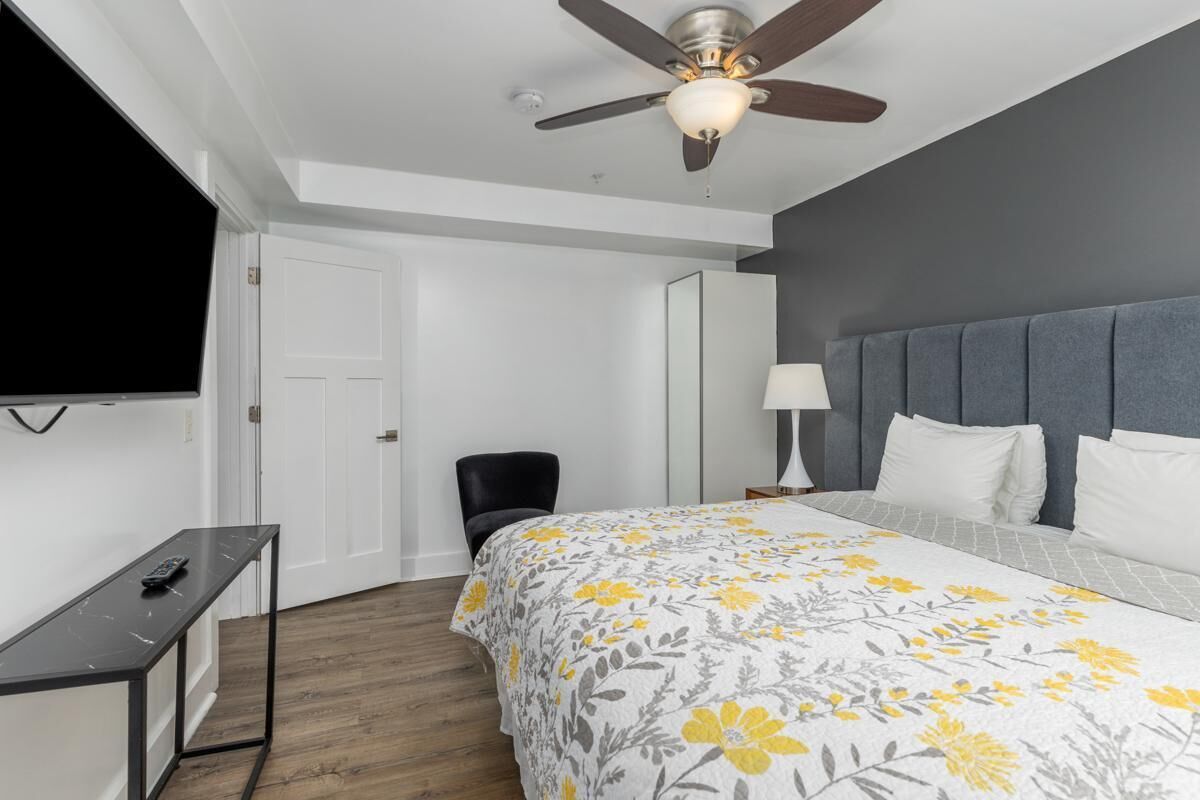 Ein Hotelzimmer mit Bett, Deckenventilator, Fernseher, Schreibtisch und Stuhl.