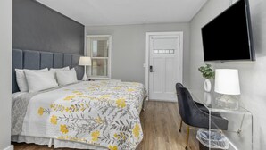 Un dormitorio con cama, mesita de noche, silla, televisor y una puerta.