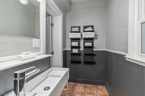 Un baño con un lavamanos blanco, un espejo y un perchero con toallas dobladas con cuidado.