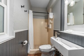Un baño con inodoro, lavamanos, espejo y zona de ducha.