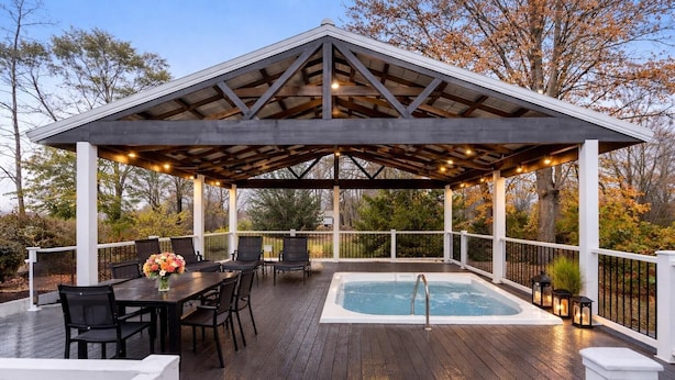 Una terraza techada al aire libre con jacuzzi, piso de madera y mobiliario exterior.