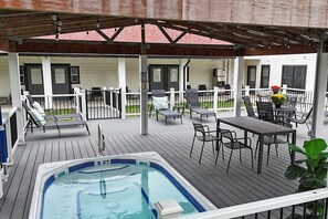 Um terraço coberto ao ar livre com hidromassagem, espreguiçadeiras e uma mesa com cadeiras.